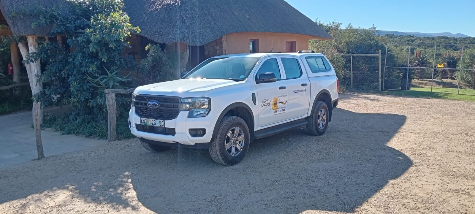 White Ford Ranger pickup truck parked in front of a thatched-roof building.