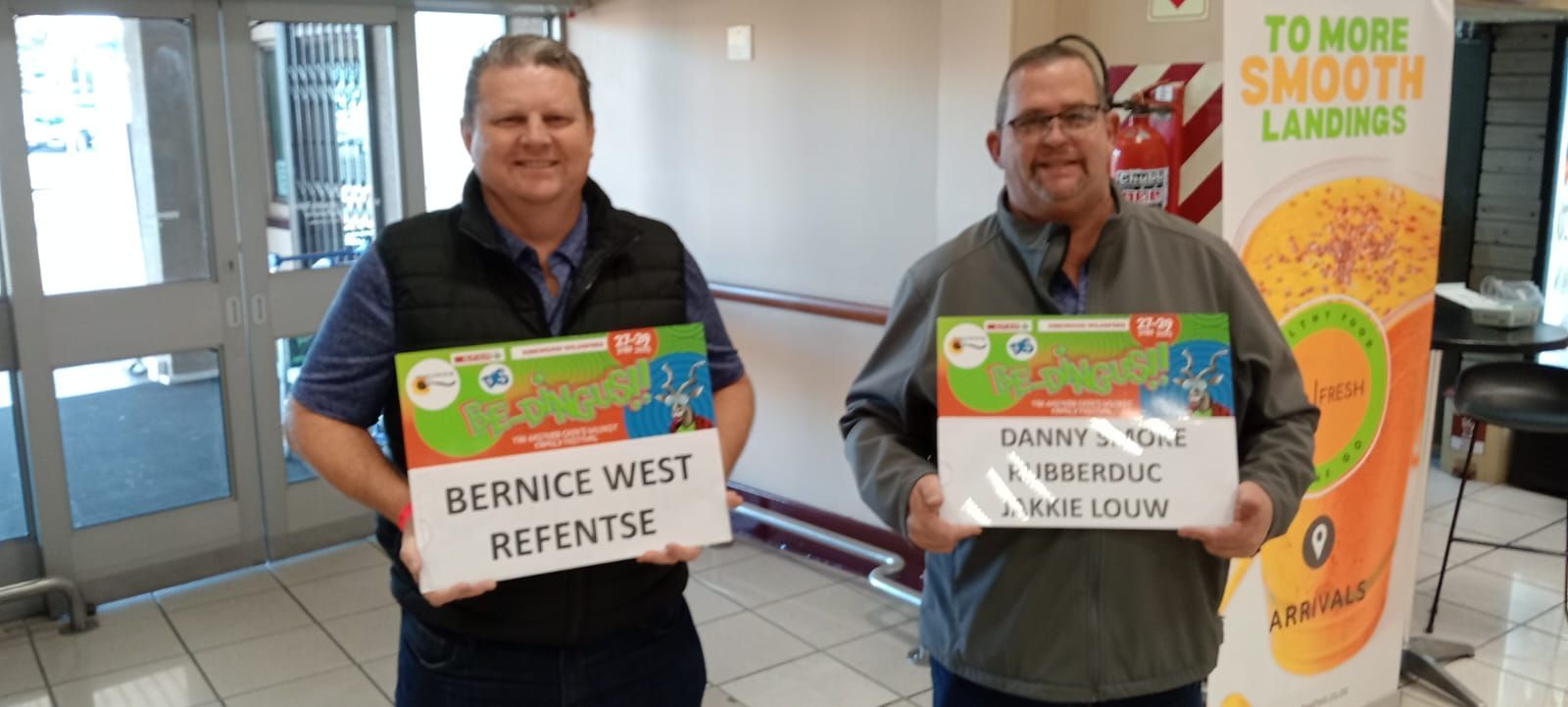Two people holding signs, smiling. One sign reads 