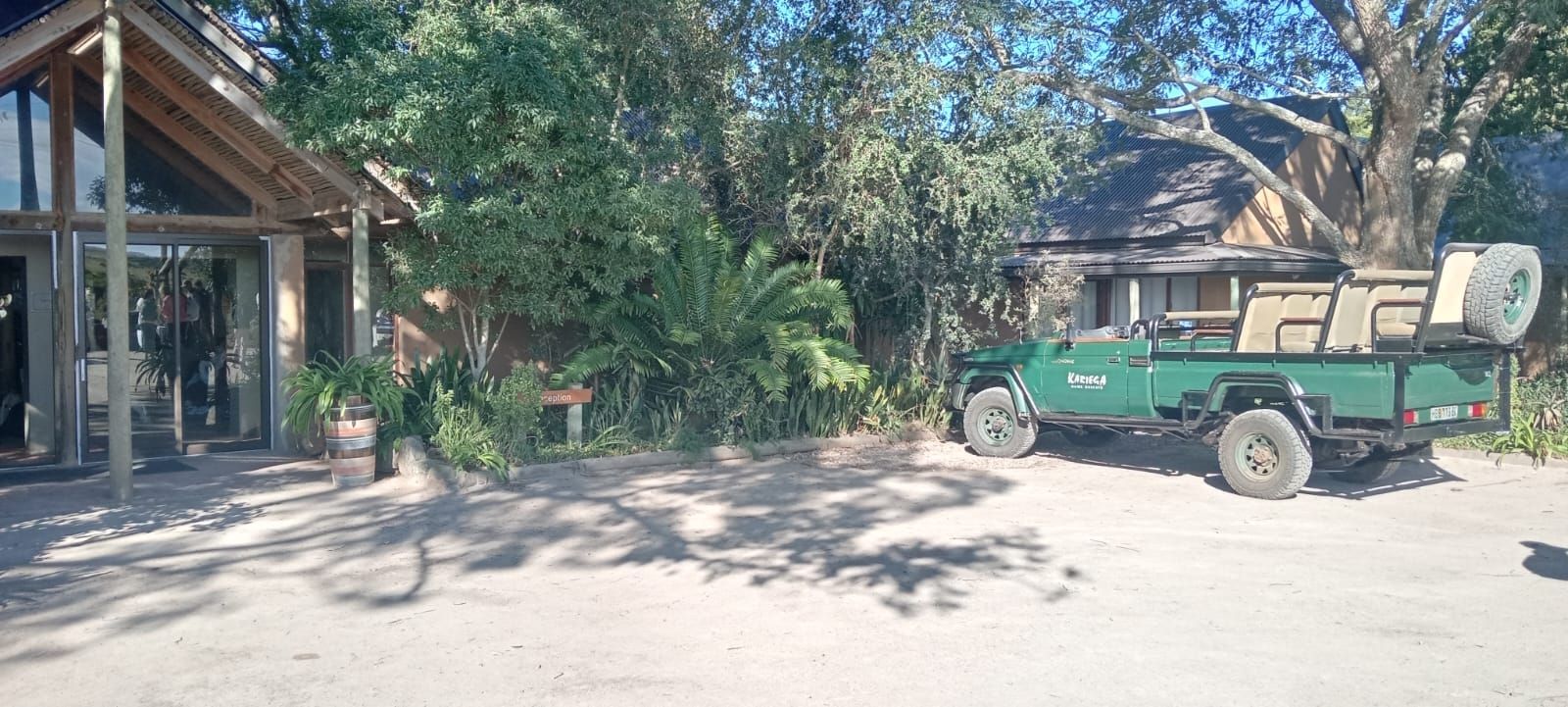 A green safari vehicle parked outside a lodge building with a thatched roof and large glass windows.