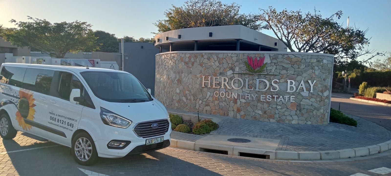 A white van parked in front of the Herolds Bay Country Estate entrance. The sign is stone with white lettering.