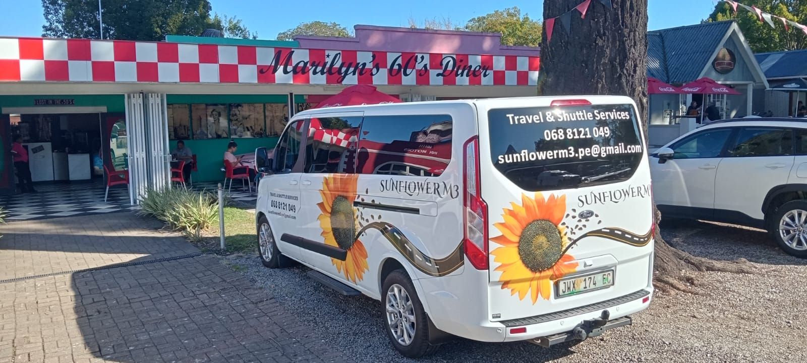 A white van with sunflower decals parked in front of a diner with a red and white checkered roof.