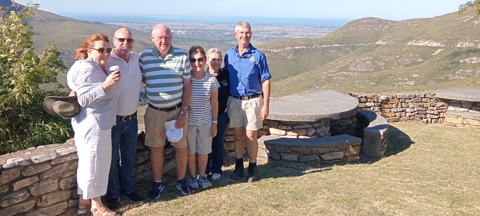 Group of people standing outdoors with mountains and a city in the background.
