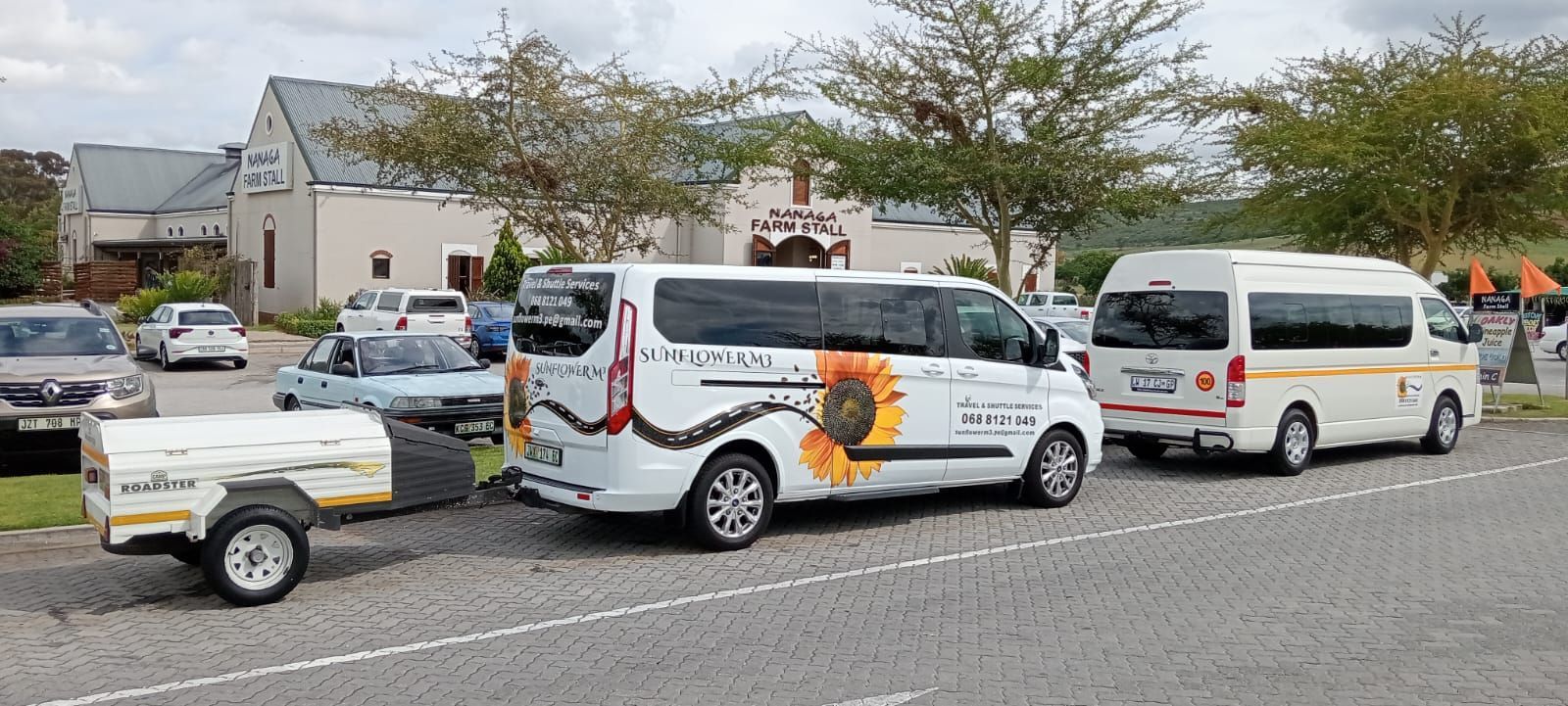 White vans and trailer parked in front of a building. One van has a sunflower design.