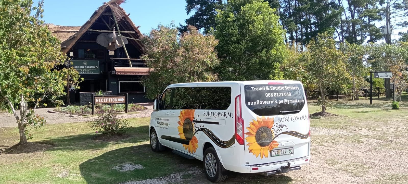 White van with sunflower design parked in front of a rustic wooden building with a thatched roof.