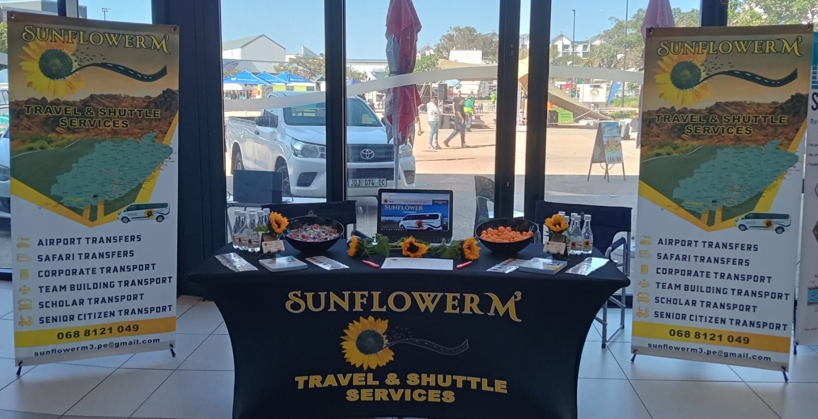 Sunflower M Travel & Shuttle Services booth with banners, display table, and sunflowers in front of a window.