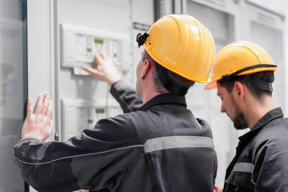 Due uomini che indossano caschi protettivi stanno lavorando su un quadro elettrico