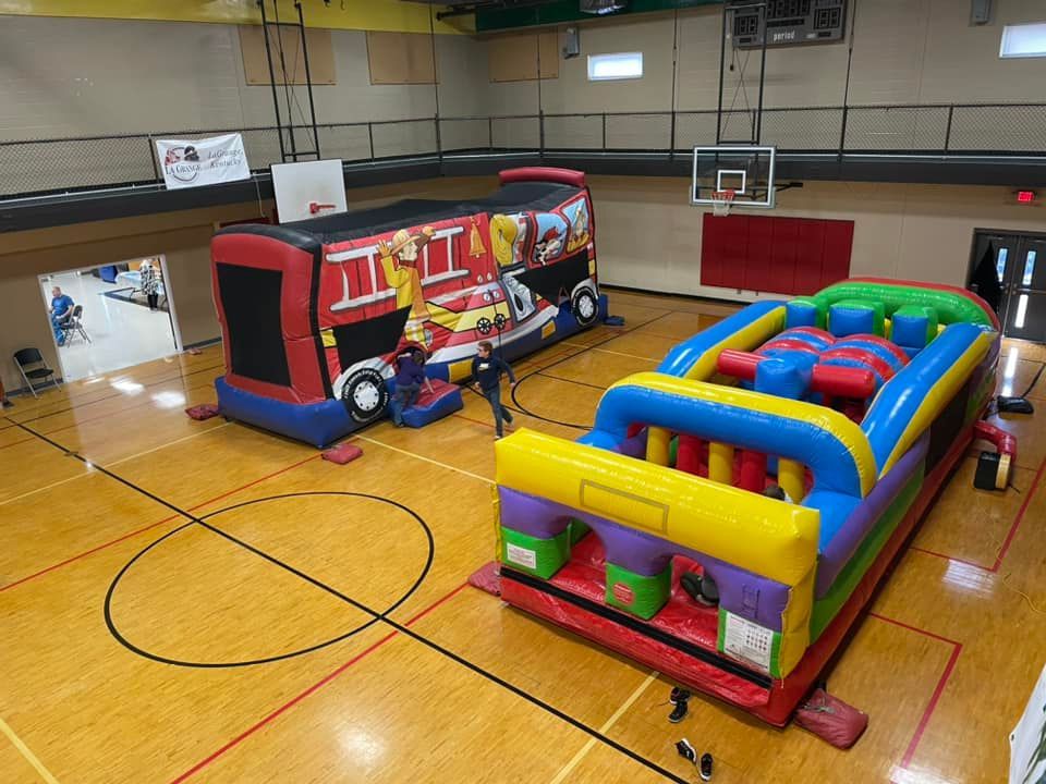 A large inflatable bouncy house and a large inflatable obstacle course are in a gym.