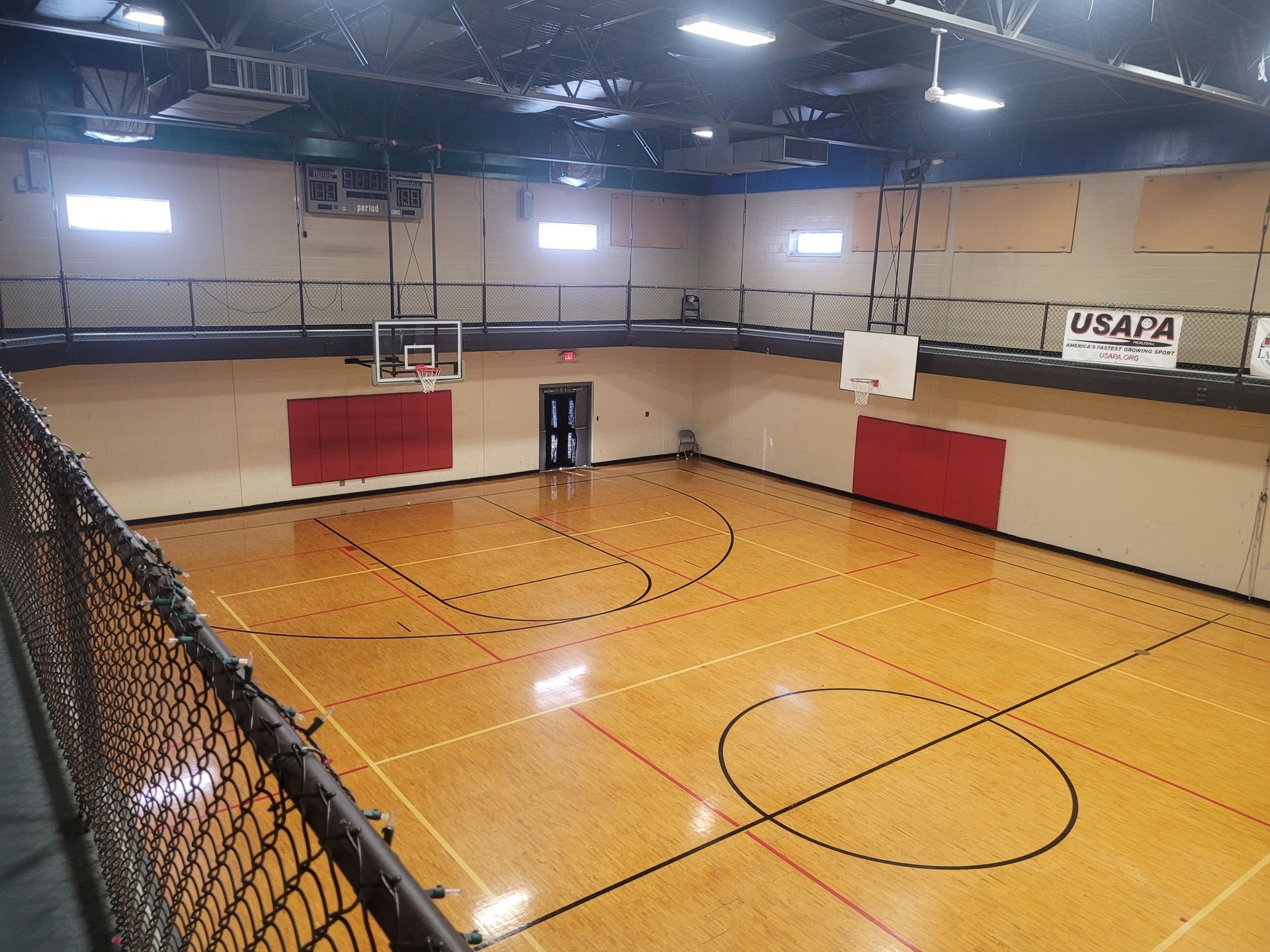 A basketball court in a gym with a fence around it.