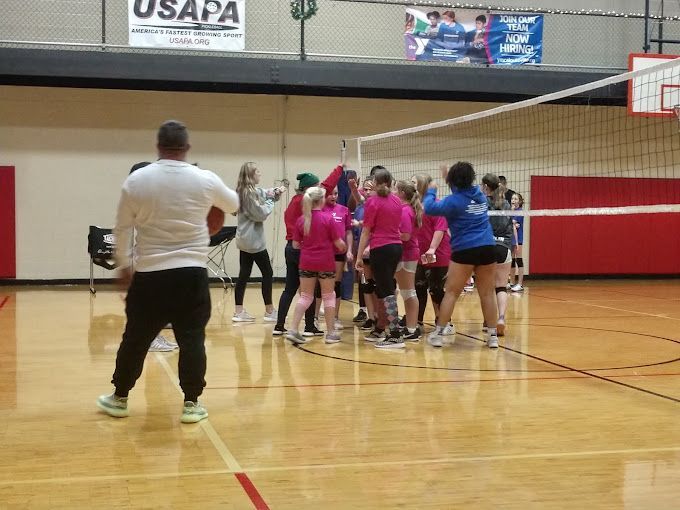 A group of people are standing around a volleyball net in a gym.