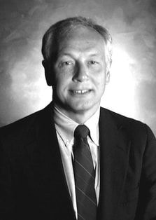 A man in a suit and tie is smiling in a black and white photo.