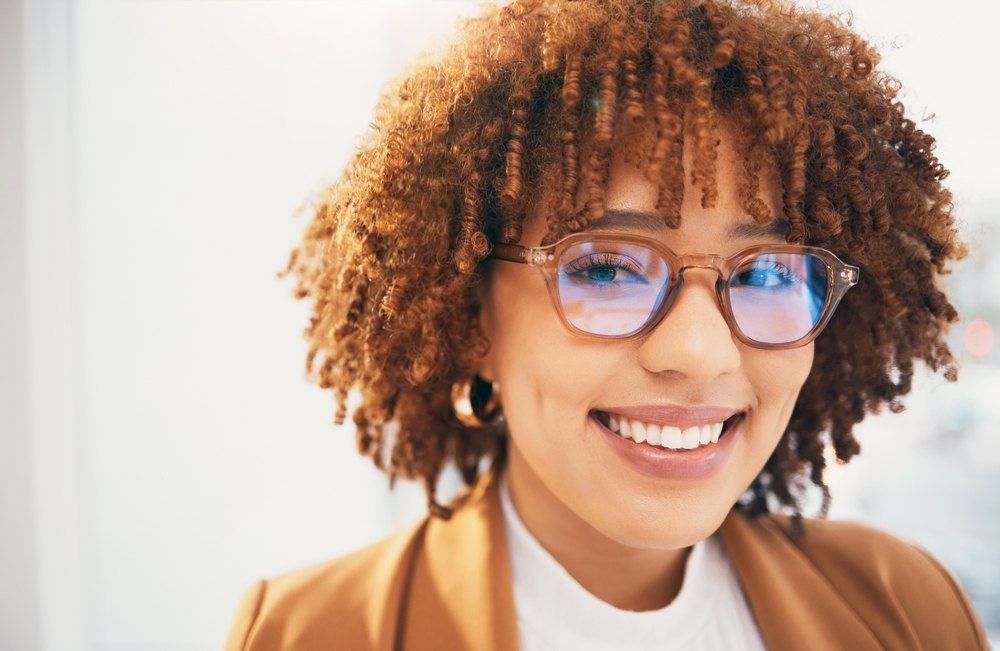 Woman With Curly Brown Hair, Smiling, Wearing Glasses — Russell Cooper Optometrist In Rockhampton QLD