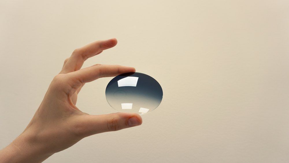 Hand Holding a Round, Blue-gradient Lens Against a Neutral Background — Russell Cooper Optometrist In Rockhampton QLD