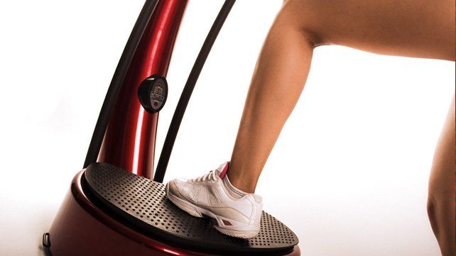 Woman's foot in a white sneaker on a vibrating exercise platform. Red machine, white background.
