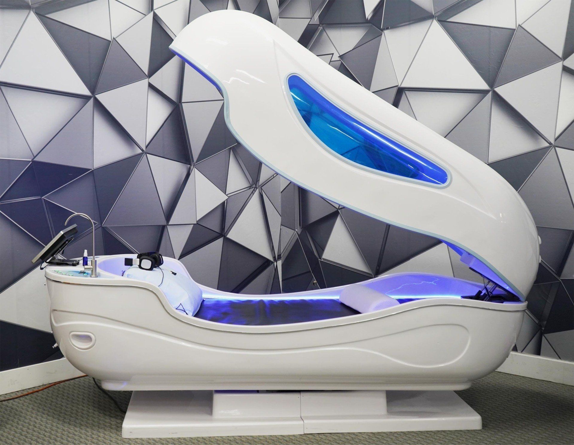 White spa capsule with blue interior lighting in front of a patterned wall.