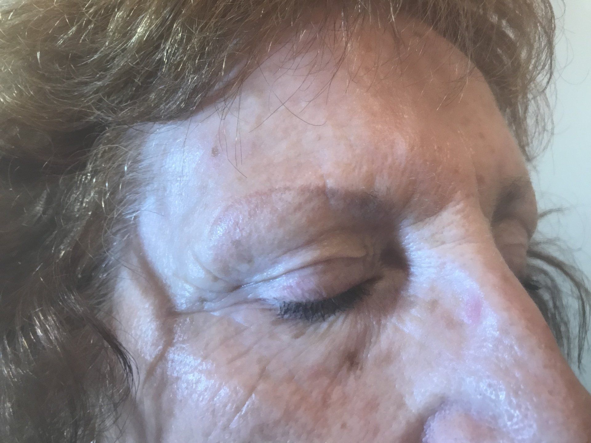 Close-up of a woman's face with closed eyes; wrinkles around the eye and forehead, light skin, fair hair.