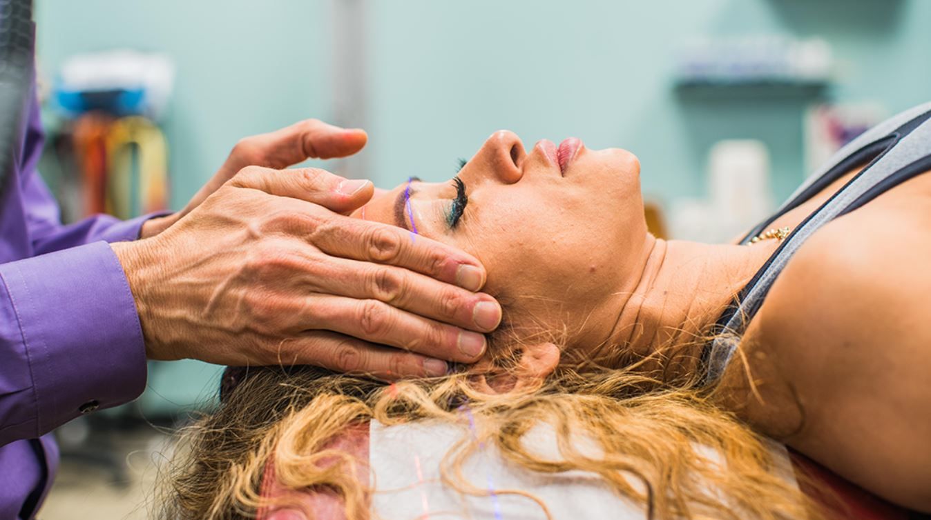 Hands gently touching a woman's forehead in a therapy session.