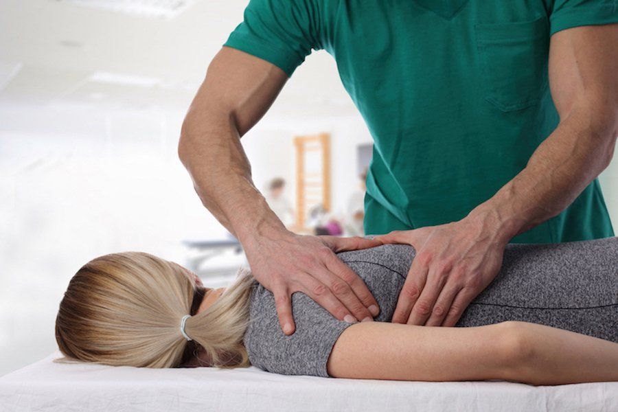 Therapist in green shirt giving massage to woman lying on a table.