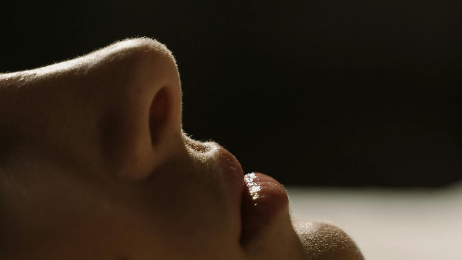 Close-up of a person's mouth and nose, lit from above, with a partially visible lip.