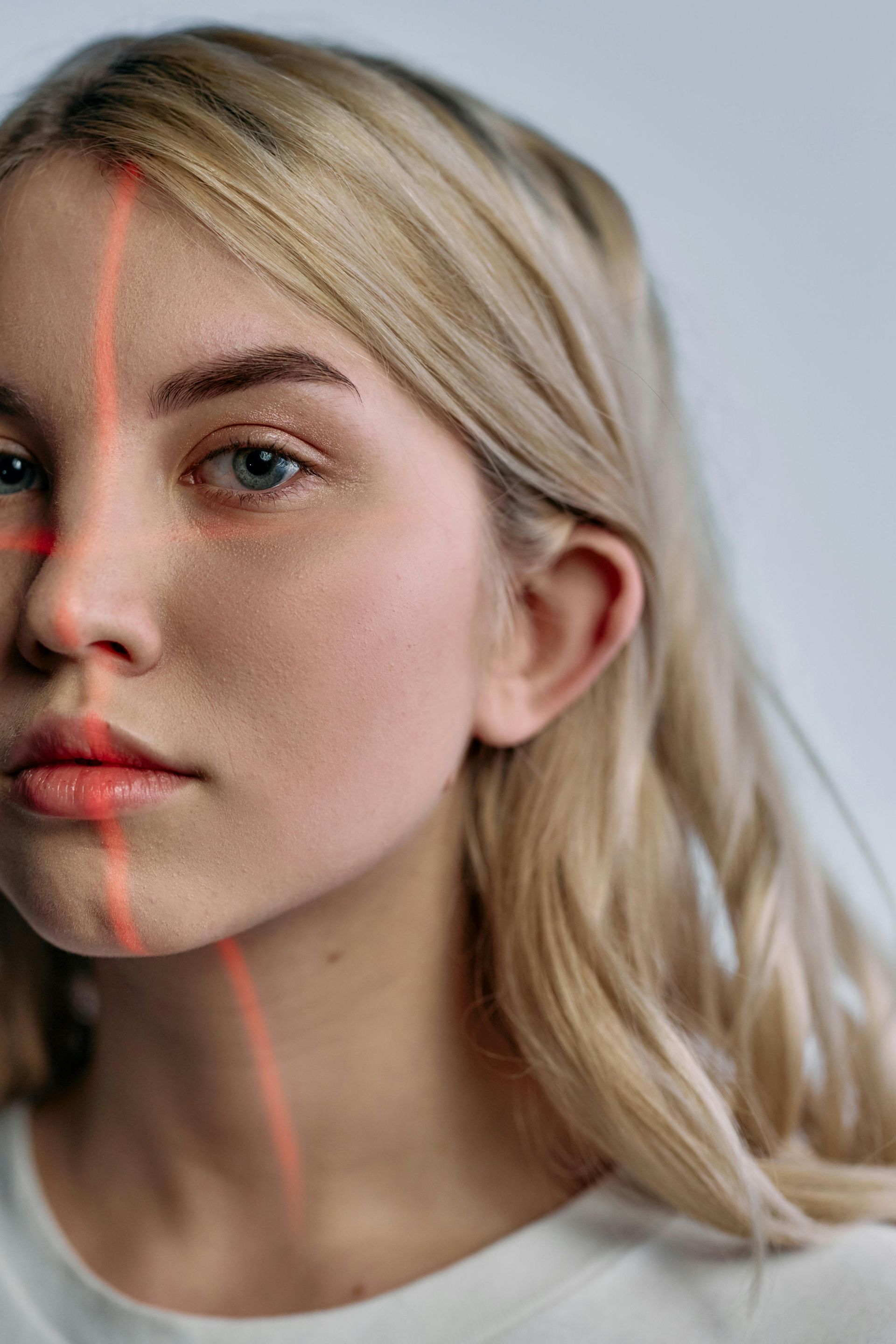 Blonde woman with red laser grid on face. Serious expression, light background.