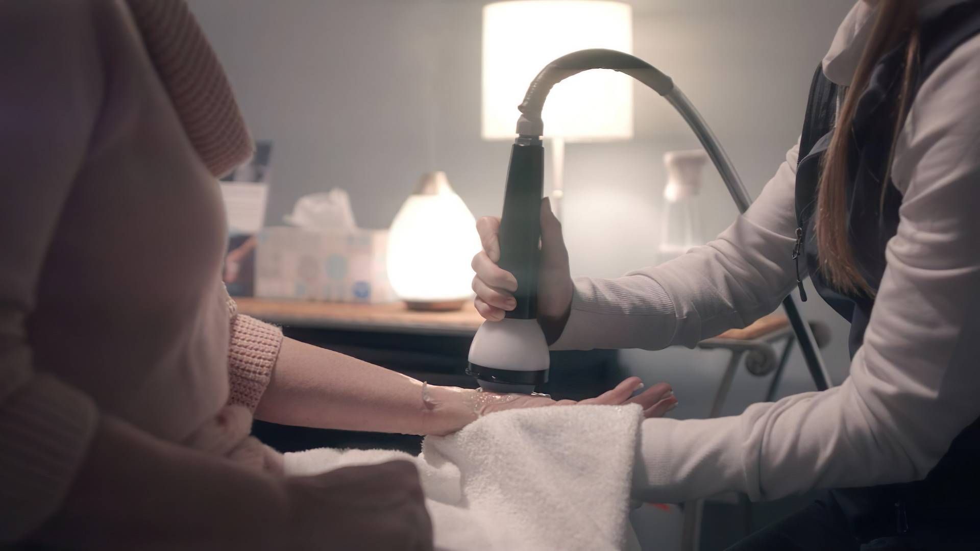 A healthcare worker uses a handheld device on a patient's arm, indoors.