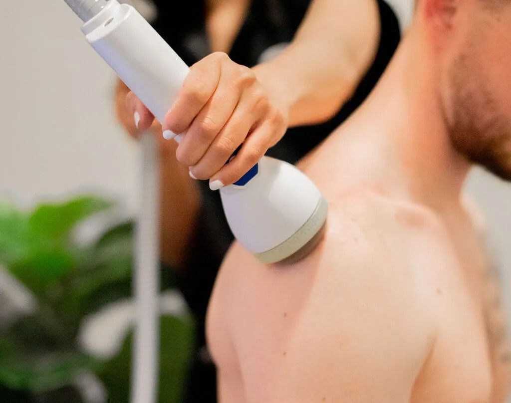 A person's shoulder being treated with a white medical device by another person in a clinic setting.