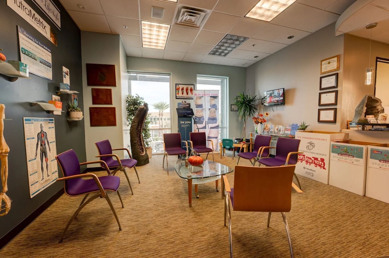 Waiting room with purple chairs, a glass table, and educational posters.