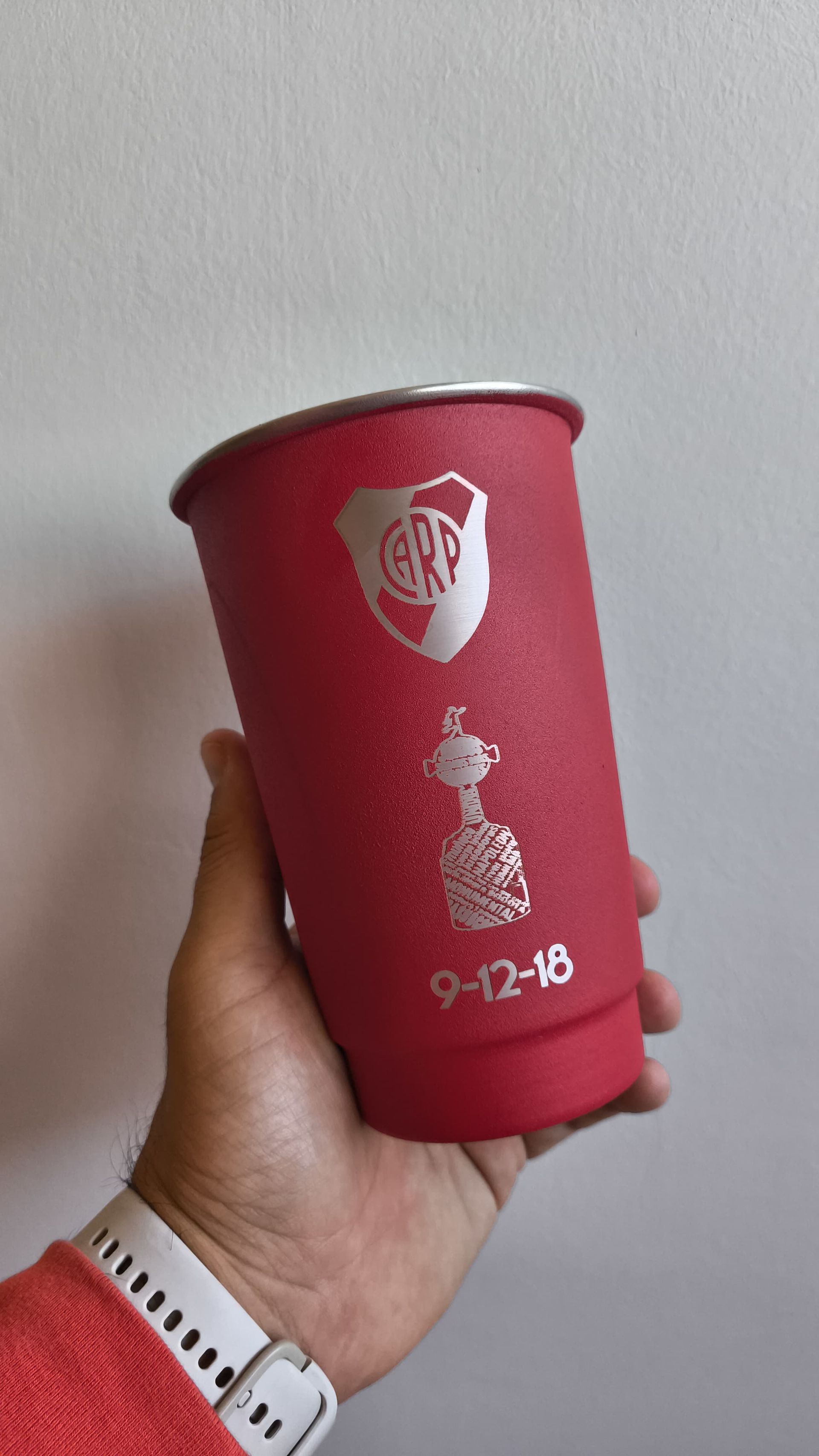 Persona sosteniendo un vaso rojo con el logo de River Plate
