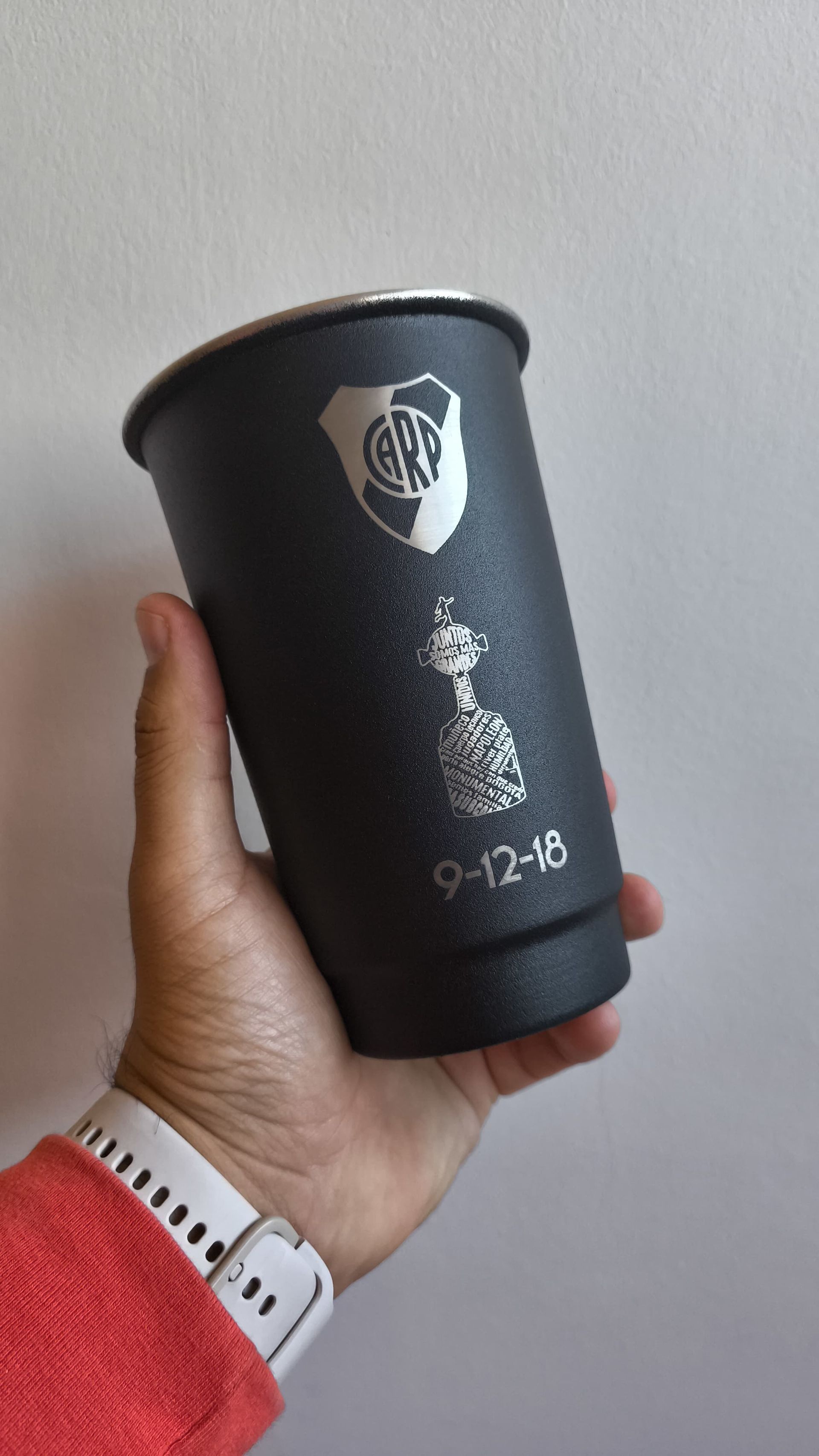 Mano sosteniendo un vaso negro con el logo de un equipo deportivo