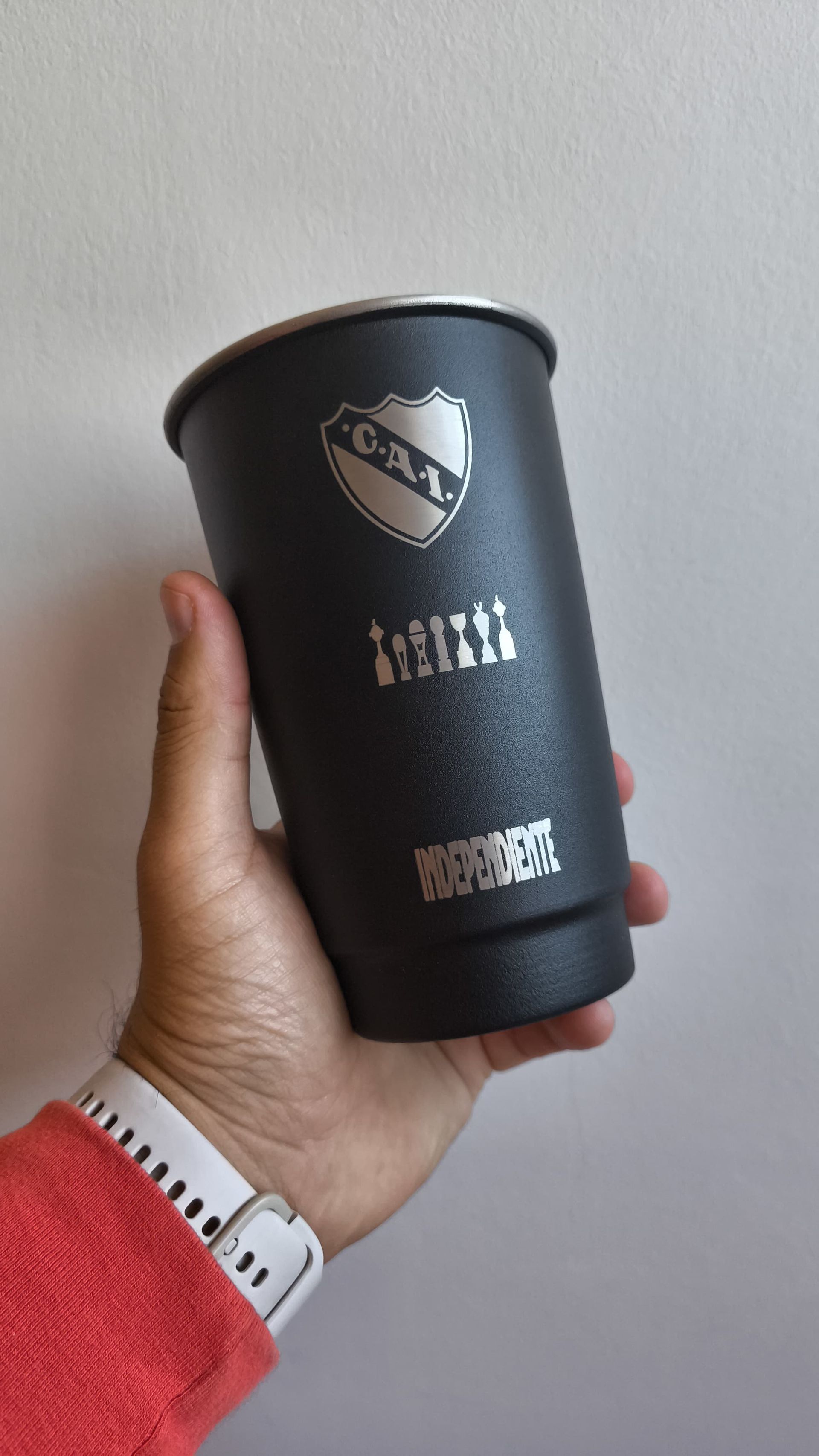 Una mano sostiene un vaso térmico negro con el logo del club "OAI".