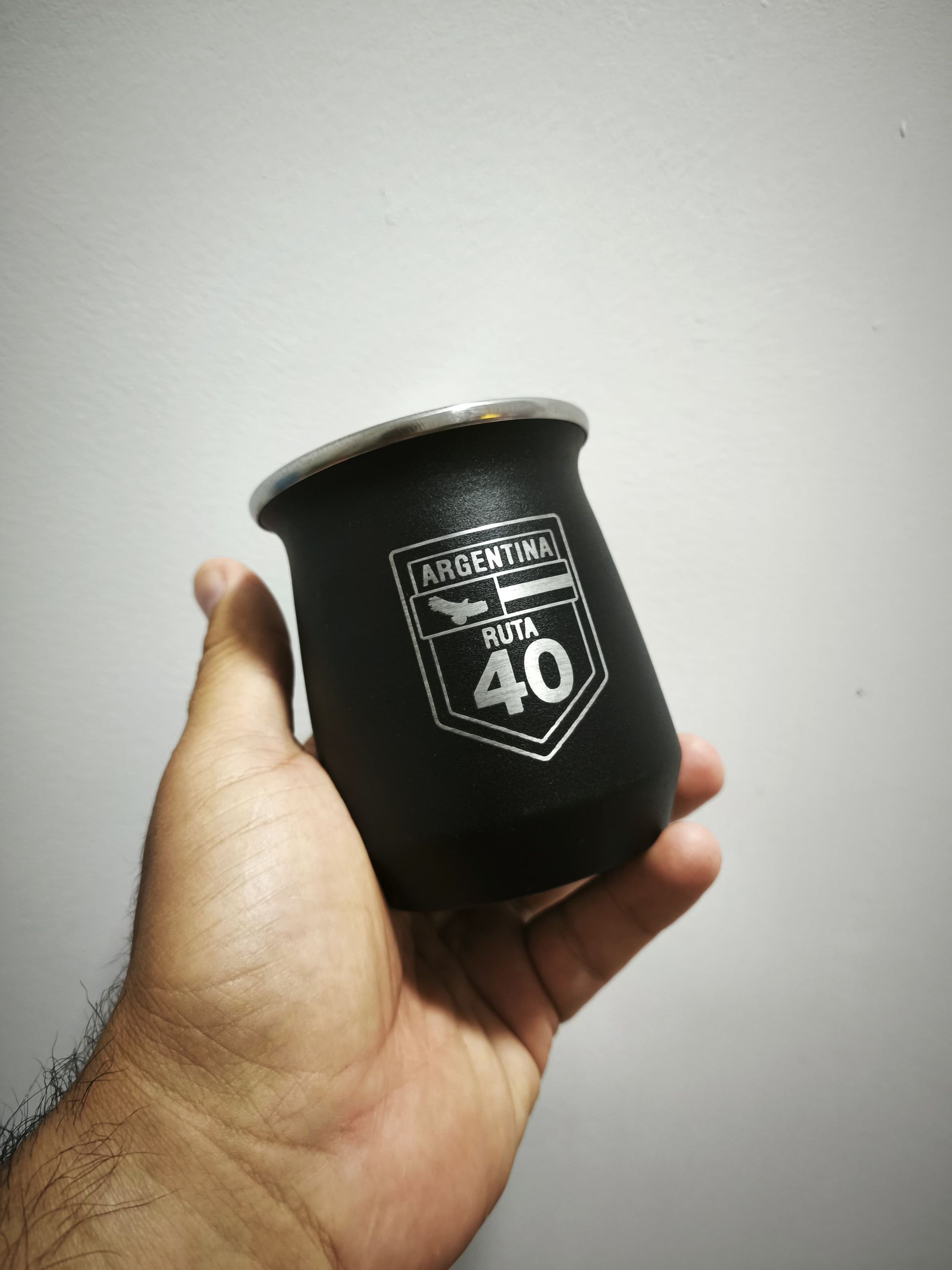 Mano sosteniendo un mate negro con la frase "Argentina Ruta 40" impresa en él.
