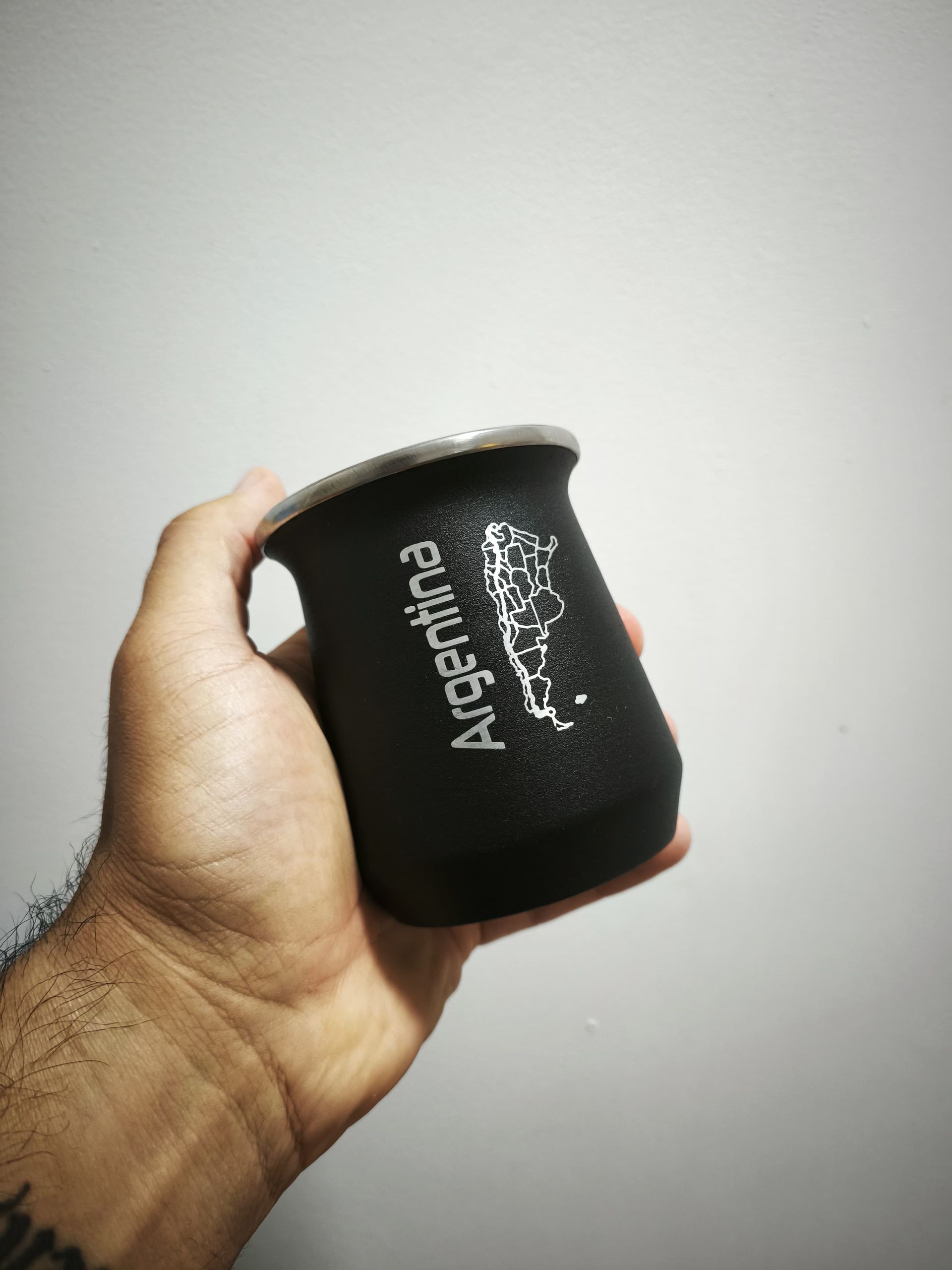 Una mano sosteniendo una calabaza mate negra con la palabra "Argentina" y un mapa del país en ella.