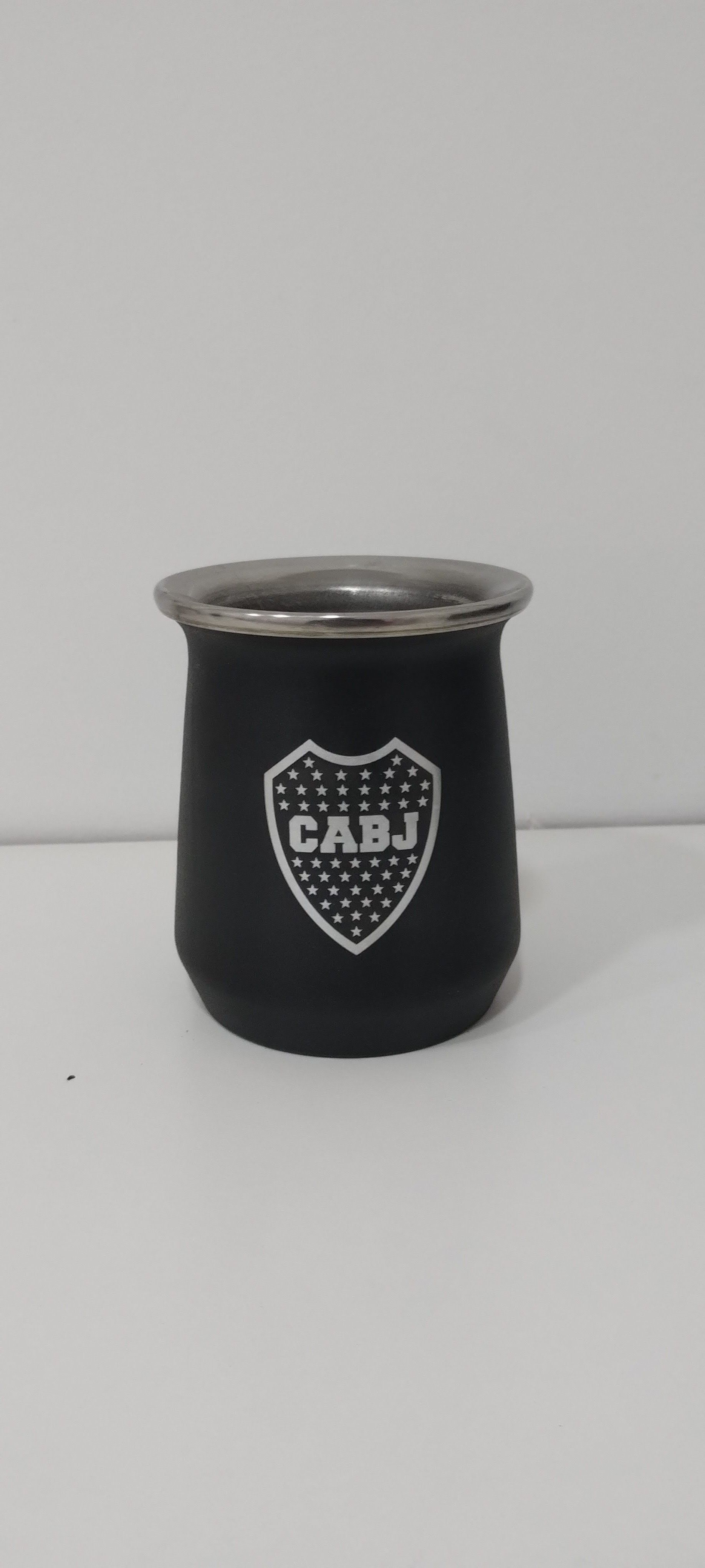Mate negro con el logo de Boca Juniors sobre superficie blanca. Borde plateado.