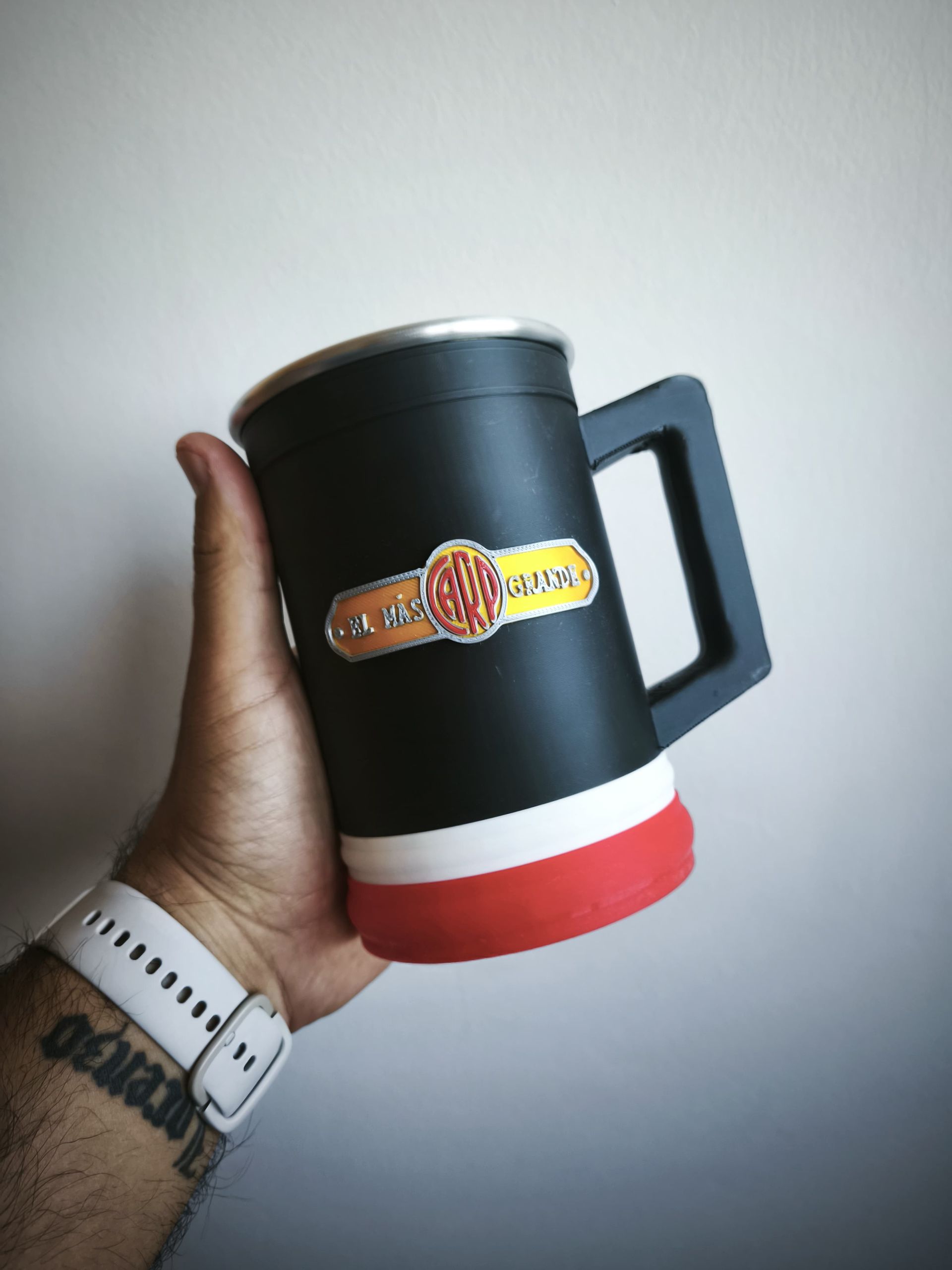 Mano sosteniendo una jarra de cerveza negra con un logotipo, detalles en blanco y rojo.