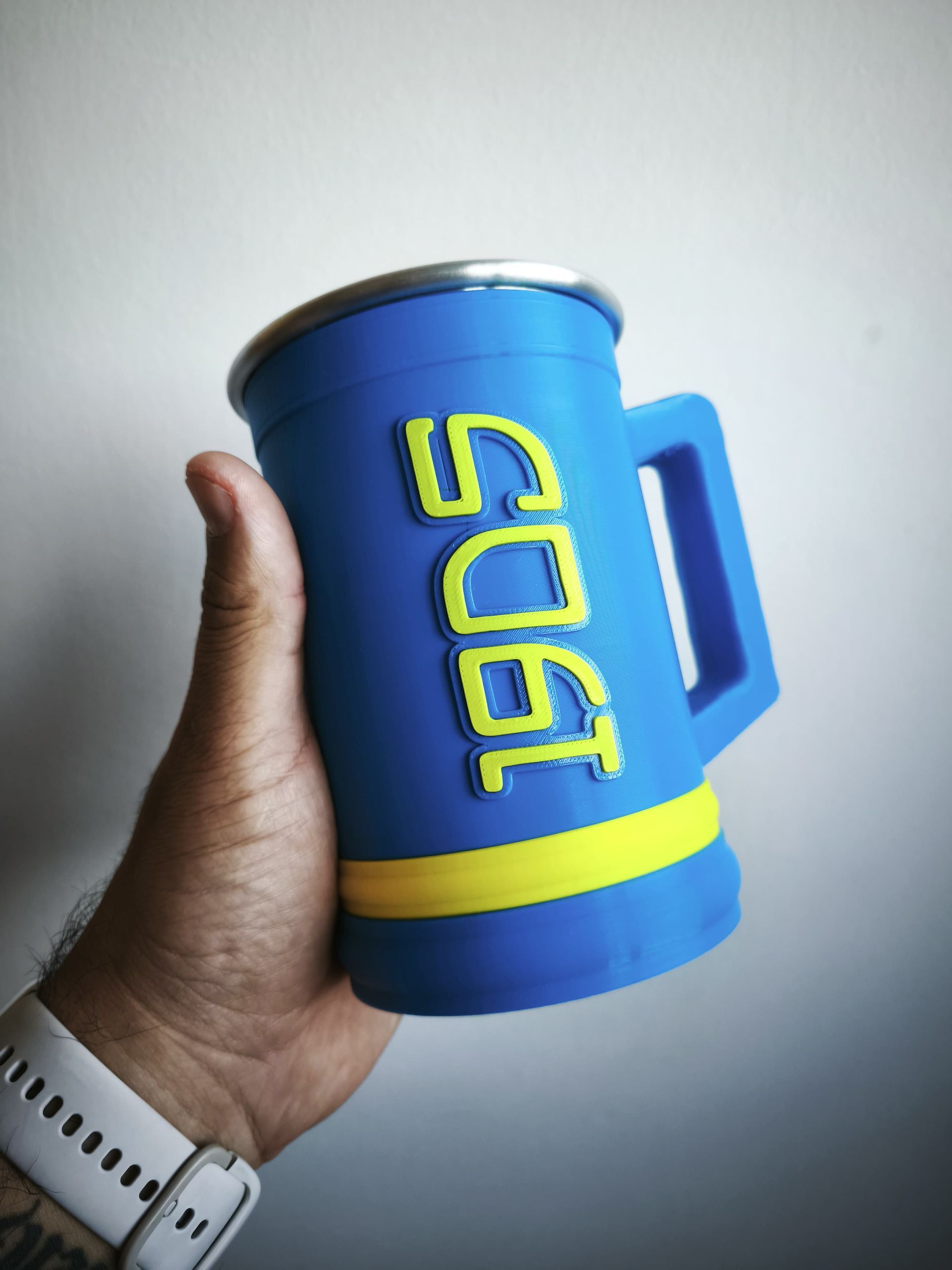 Una persona sosteniendo una jarra de cerveza azul de Boca Juniors con detalles amarillos y el logo del club.