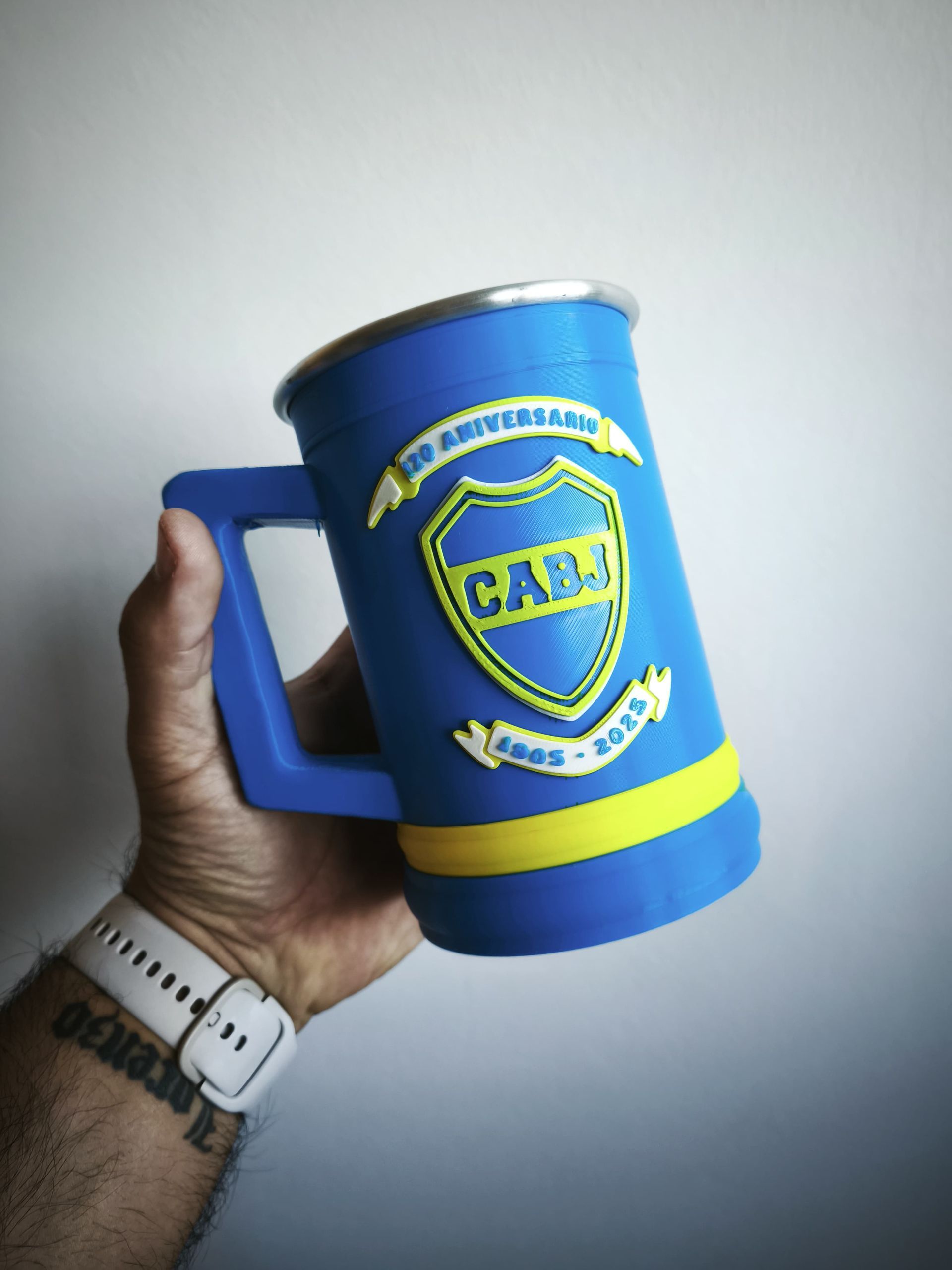 Una persona sosteniendo una jarra de cerveza azul de Boca Juniors con detalles amarillos y el logo del club.