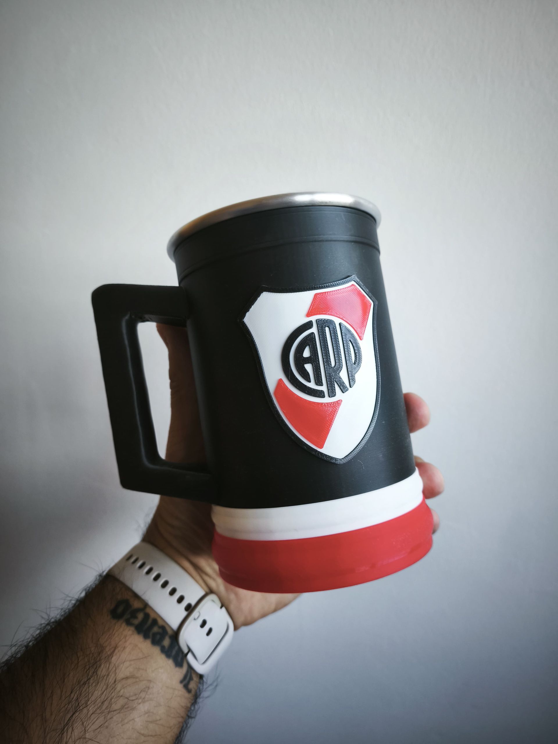 Mano sosteniendo una jarra de cerveza negra con un logotipo, detalles en blanco y rojo.