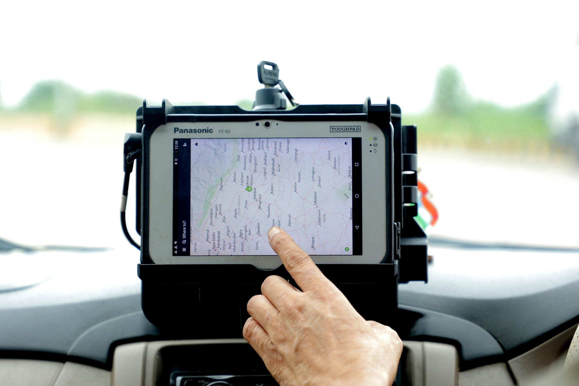 A hand pointing at a tablet showing a map, mounted on a car dashboard.