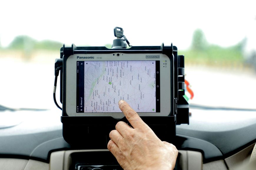 A hand pointing at a tablet showing a map, mounted on a car dashboard.