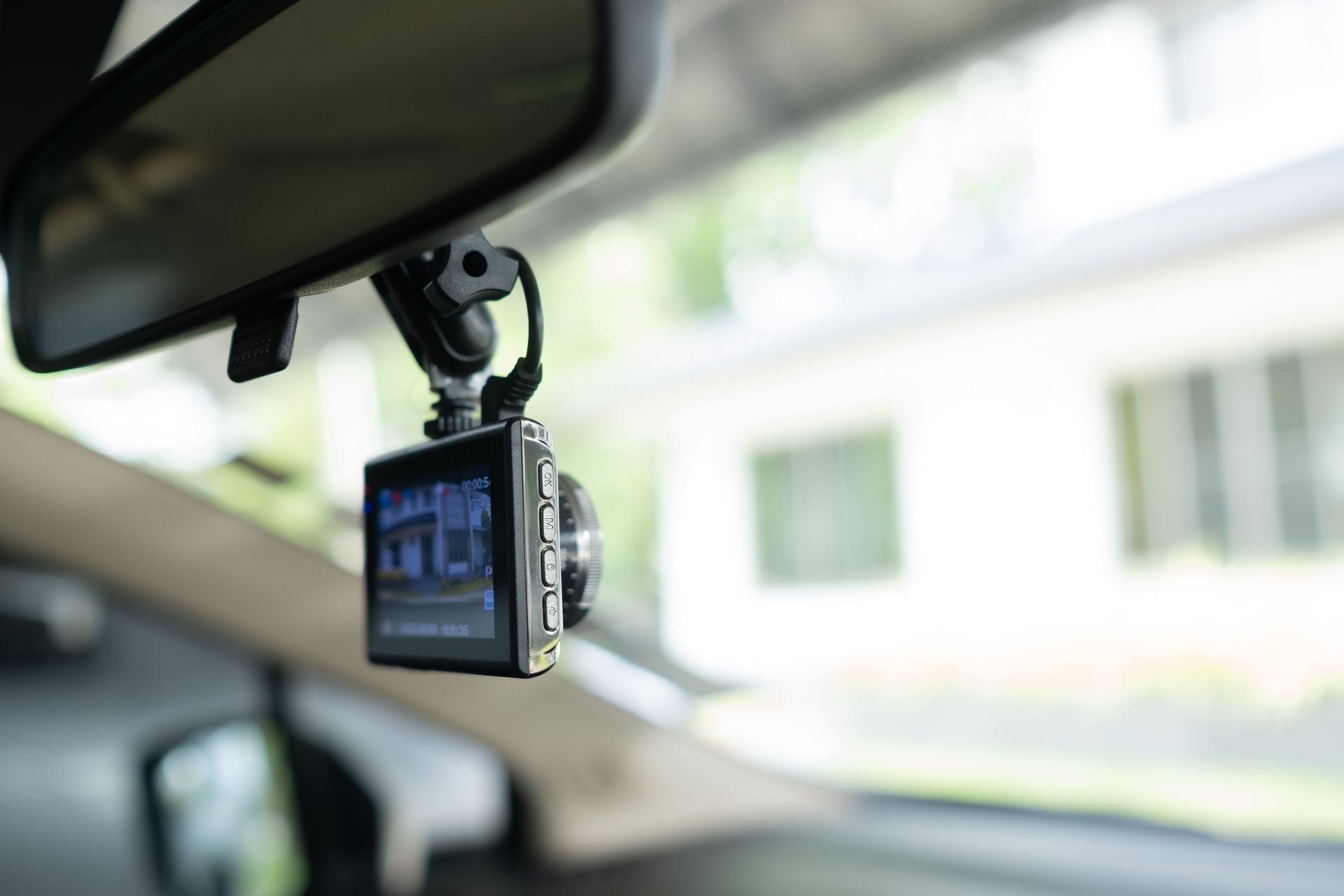 Dashcam hanging from a car's rearview mirror, displaying a street scene on its screen.