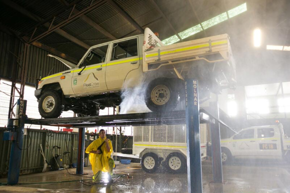 A worker in a yellow suit washes a white pickup truck on a lift in a garage. — Mt Isa Four Wheel Drive Services in Mount Isa City, QLD