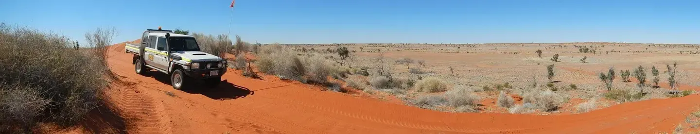 A White Suv Drives Along a Red Dirt Track in a Desert Landscape — Mt Isa Four Wheel Drive Services in Mount Isa City, QLD