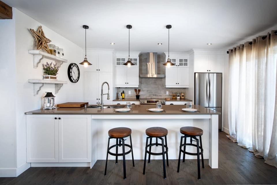Une cuisine avec des armoires blanches, des tabourets, un réfrigérateur et un grand îlot.