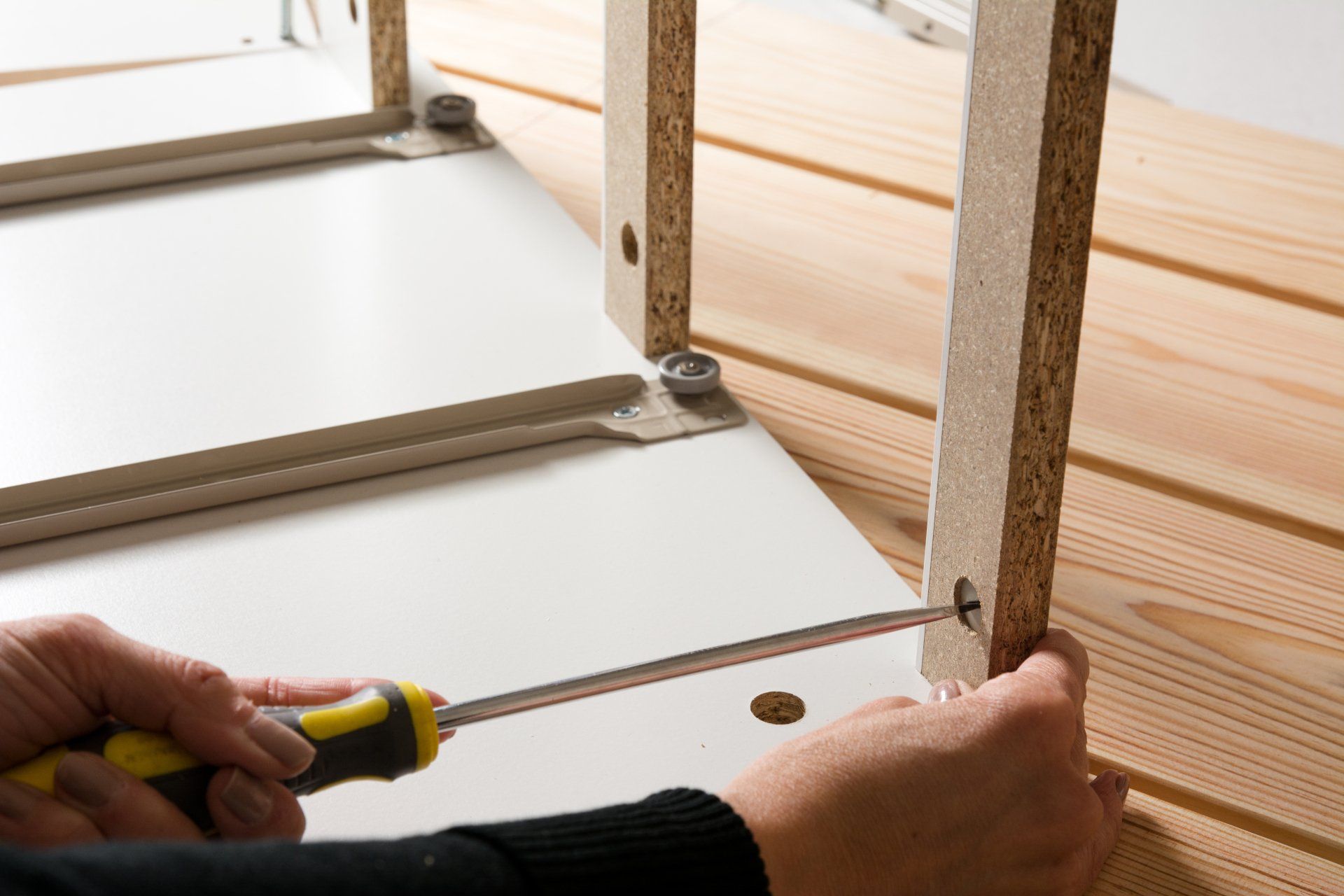 Une personne tient un tournevis et mesure un morceau de bois.