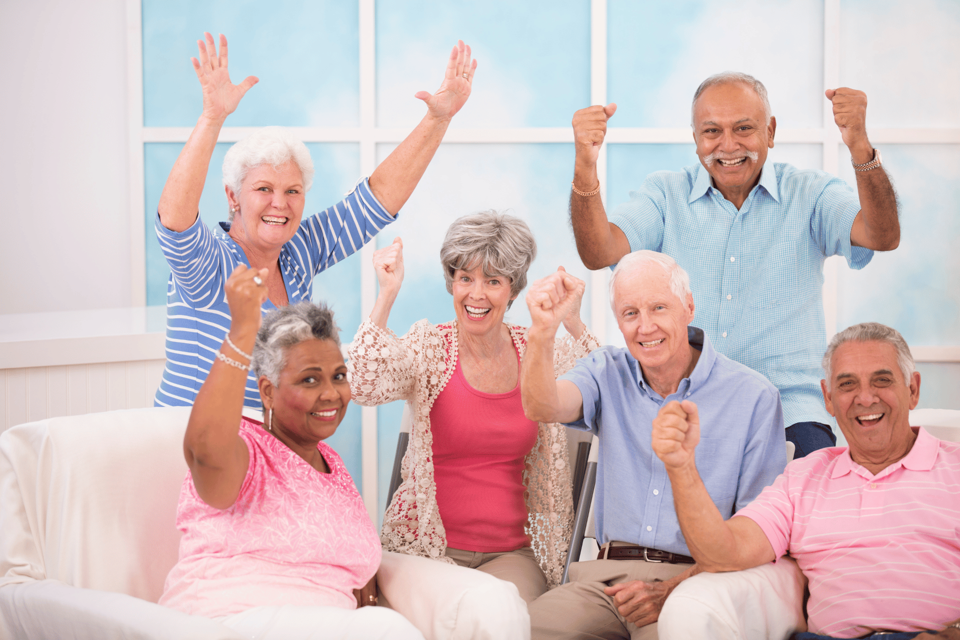 A group of elderly people are sitting on a couch with their hands in the air.