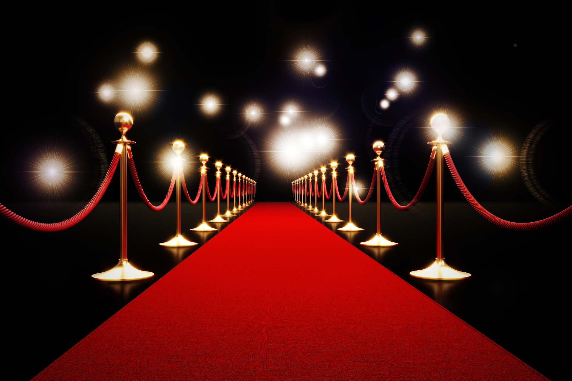 A red carpet is lined with rope barriers and lights.