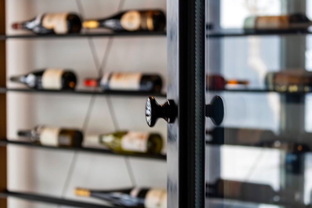 wine cellar refrigeration near m Black wine cabinet with glass door and black knob, showcasing wine bottles on shelves.