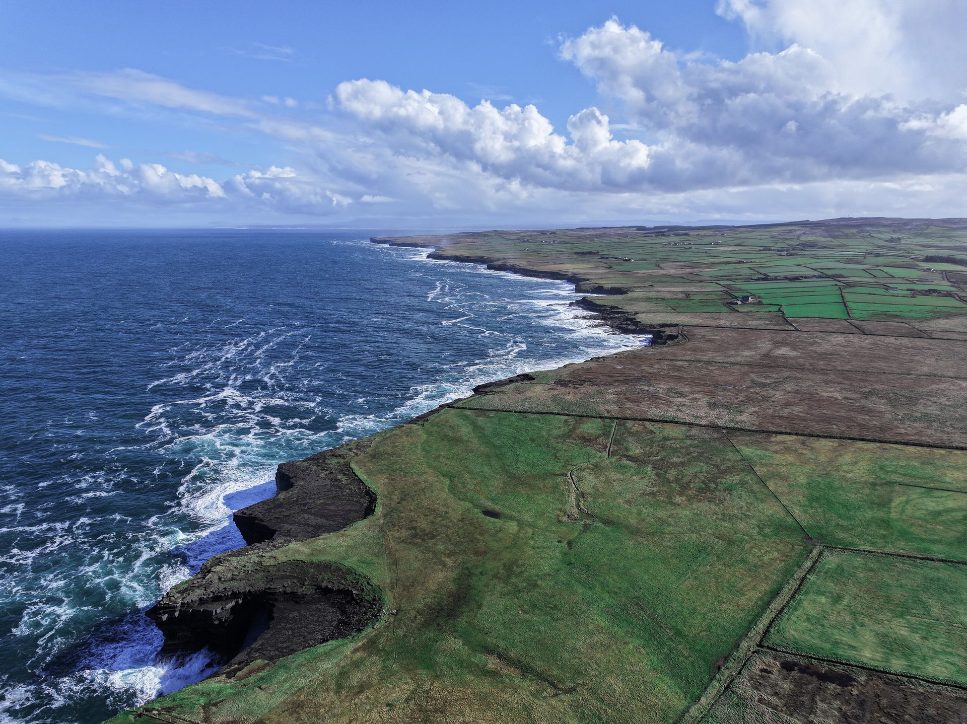 An aerial view of a cliff overlooking the ocean and a grassy field.