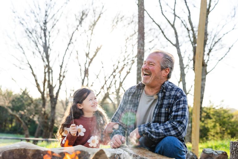 A man and a little girl are sitting around a campfire.
