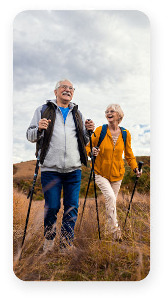A man and a woman are walking through a field with walking poles.