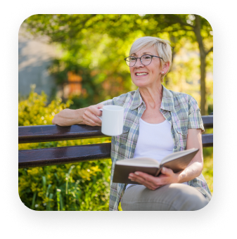 A woman is sitting on a bench reading a book and holding a cup of coffee.